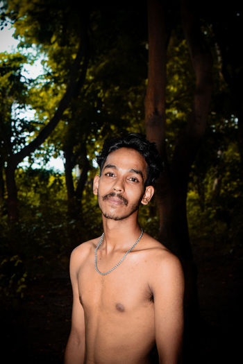Portrait of shirtless man standing against trees in forest