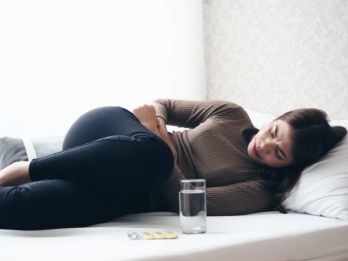 Woman with stomachache lying down on bed at home