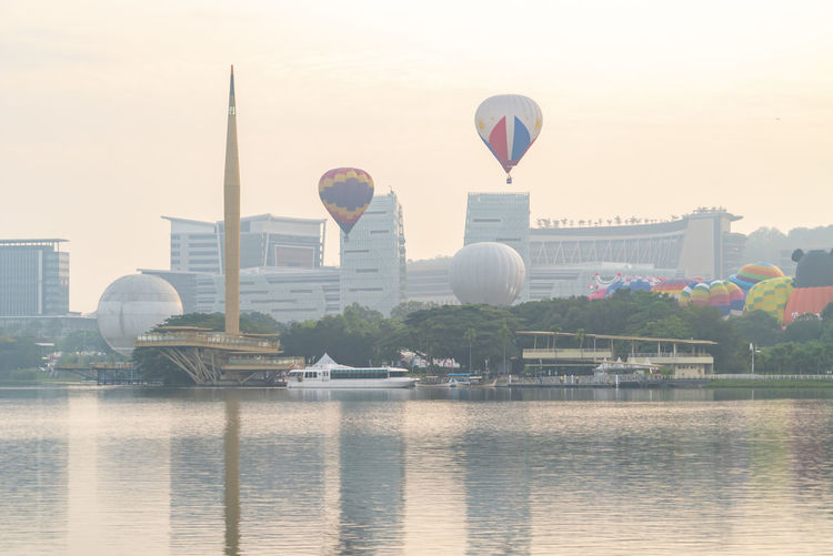Hot air balloon flying over river with buildings in background
