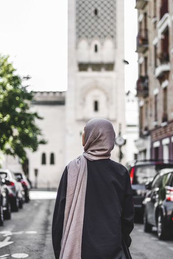 Rear view of woman standing on street with mosque
