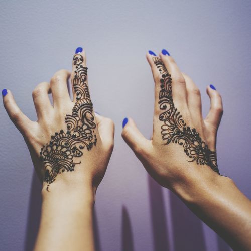 Cropped hands of woman with henna tattoo by wall