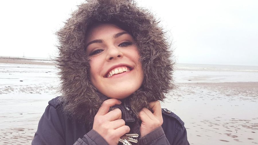 Portrait of smiling woman wearing fur coat at beach during winter