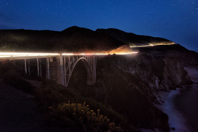 Illuminated arch bridge over river against sky at night