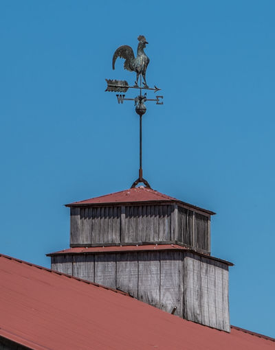 Rooster weather vane on top of a cupola with a red roof pointing to the direction of the wind 