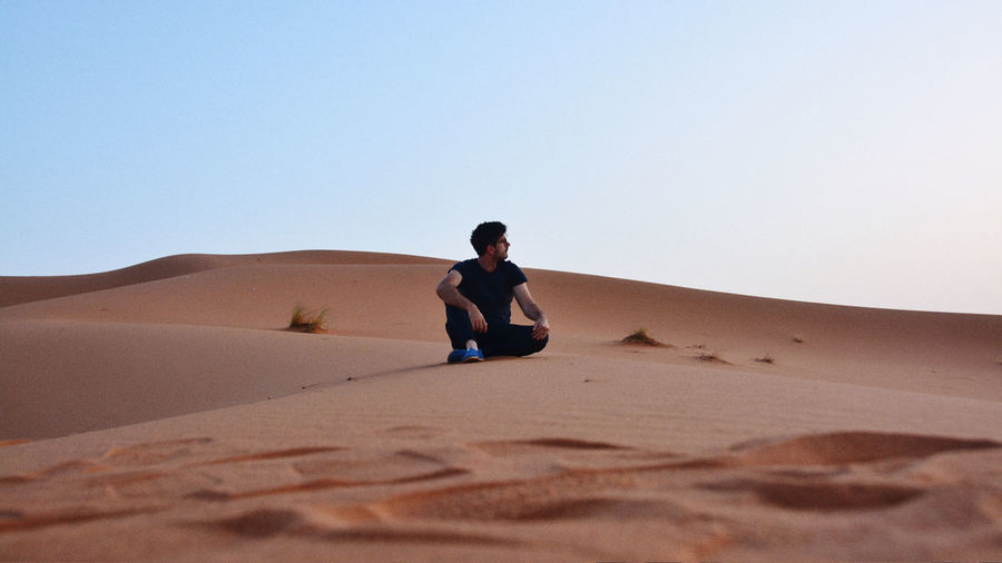 Full length of man on sand dune in desert against clear sky