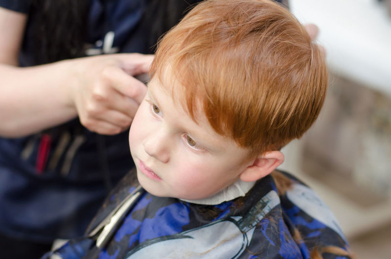 The hands of the hairdresser are cutting the boy's hair with a trimmer.