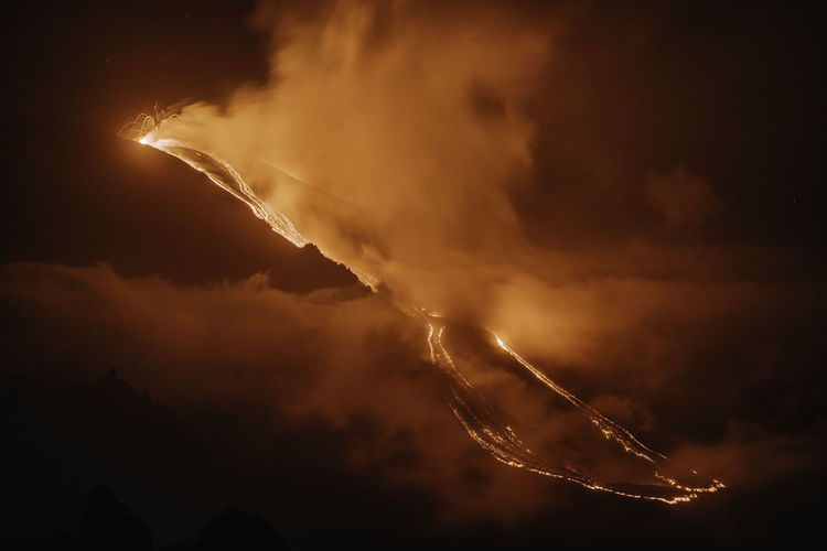 Smoke emitting from volcanic eruption against sky at night