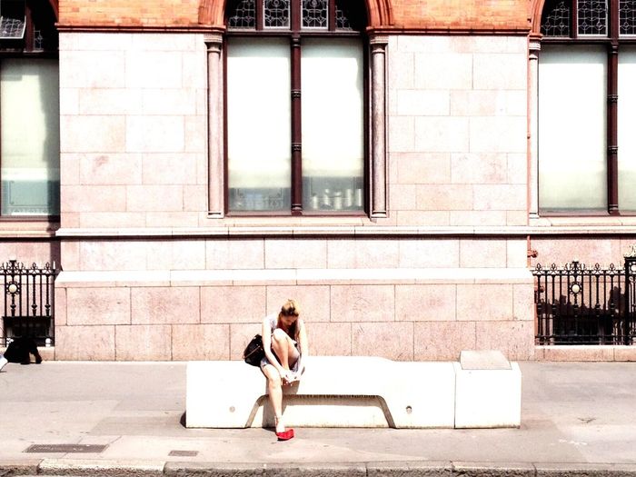 Woman sitting on sidewalk against building