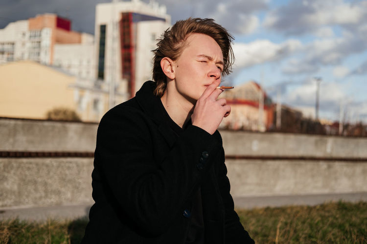 Young man smoking cigarette while sitting outdoors