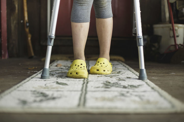 Low section of girl with crutches standing on rug at home