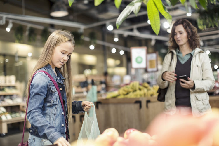 Mother looking at daughter buying apples in supermarket
