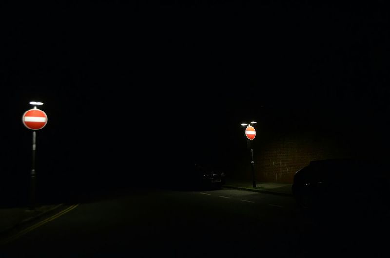 Illuminated road sign against sky at night
