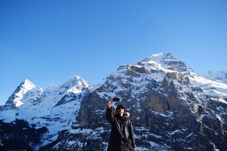 Man taking a selfie on snowcapped mountain against clear blue sky