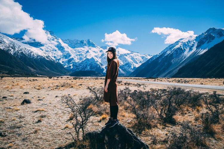 Full length of young woman standing on snowcapped mountain