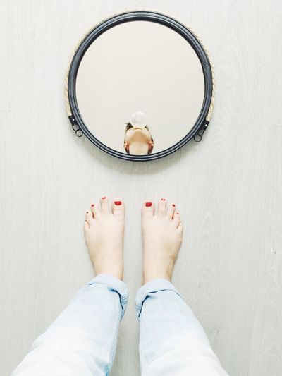 Low section of woman standing against mirror with reflection on floor