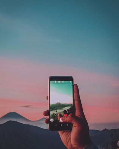 Man photographing using smart phone against sky during sunset