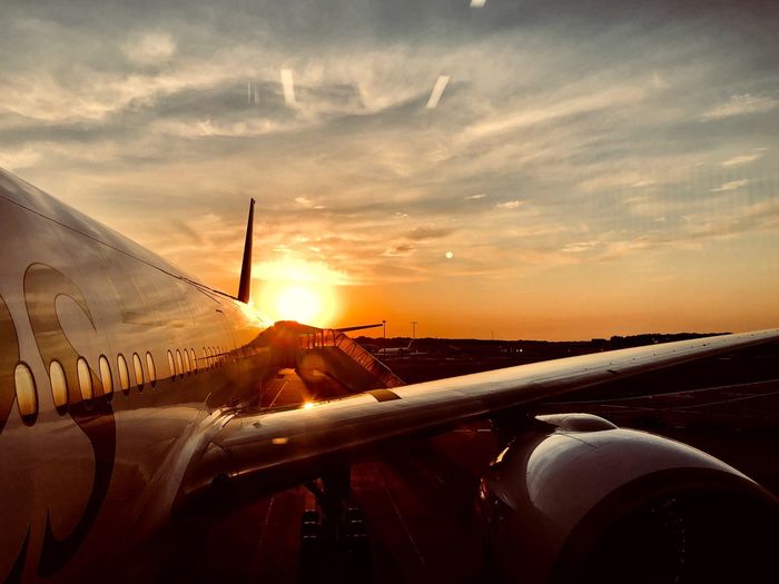 Airplane at airport runway against sky during sunset