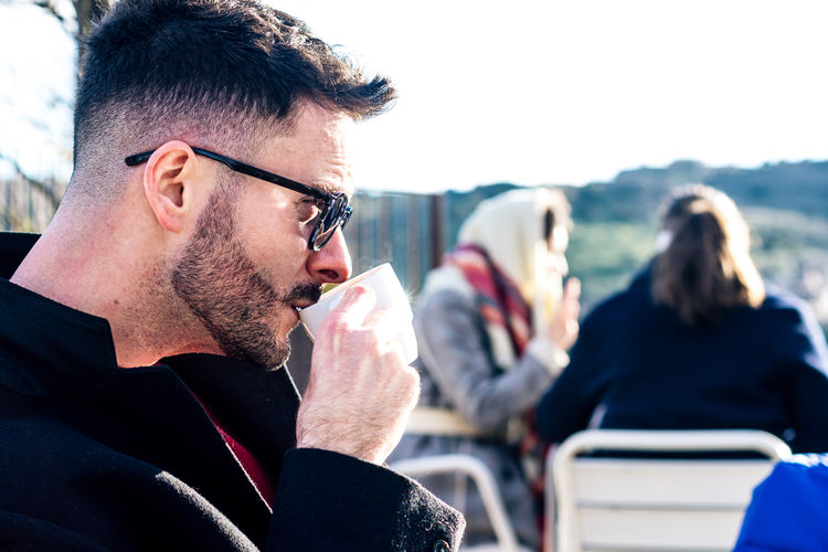 Side view of handsome man wearing sunglasses drinking coffee