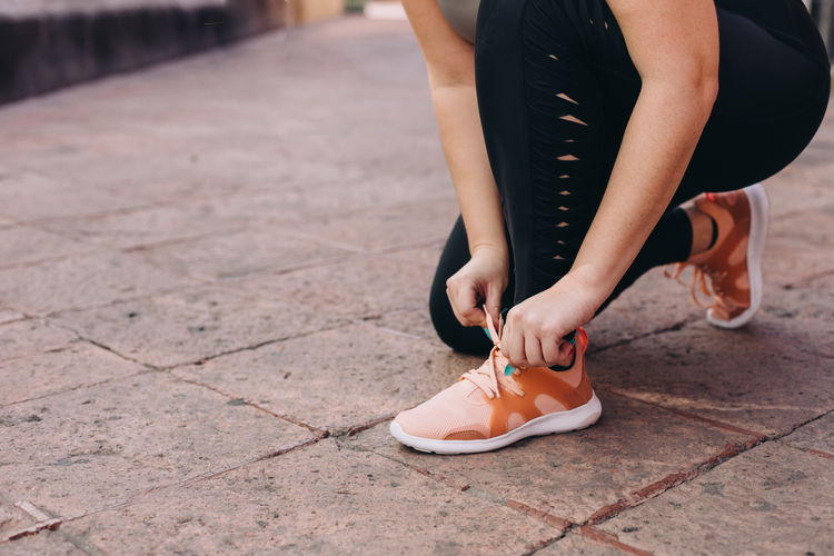 Low section of woman tying shoelaces on footpath