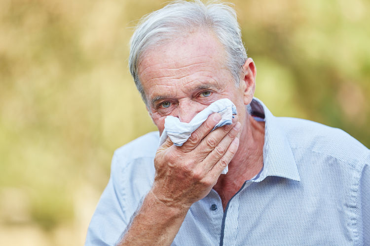 Portrait of senior man covering mouth with napkin in park