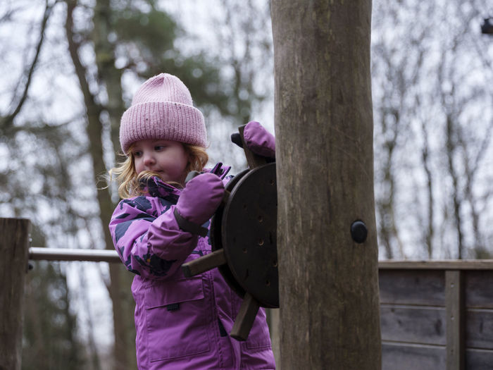 Girl in pink winter clothes holding rudder on playground