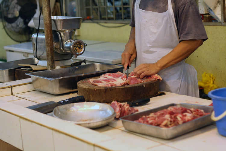 Midsection of butcher cutting meat at shop