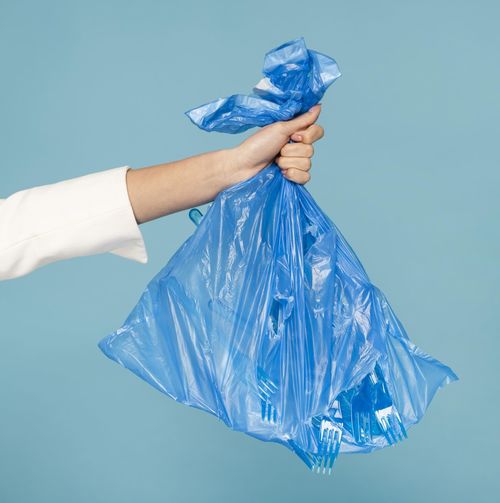 Cropped hand of woman holding plastic bag against blue background