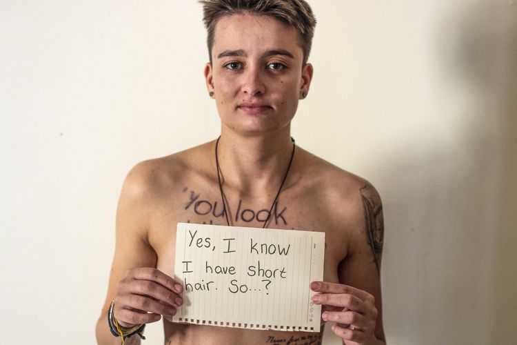 Portrait of shirtless young woman showing paper with text against wall