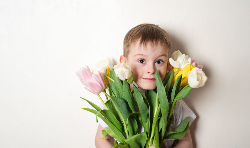 Portrait of cute girl holding flower against white background