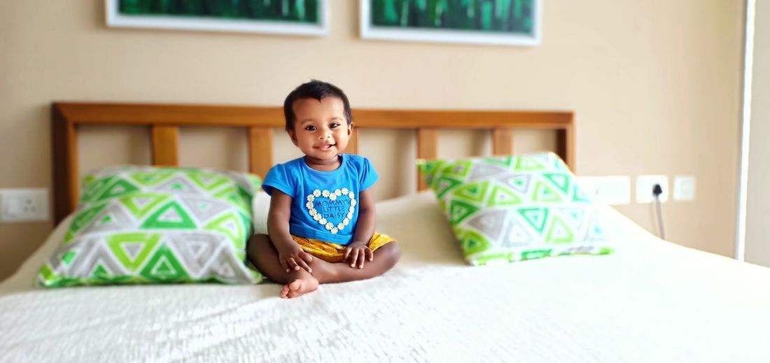 Cute smiling baby girl sitting on bed at home