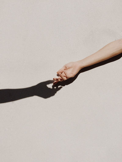 Cropped hand of woman gesturing with shadow against wall