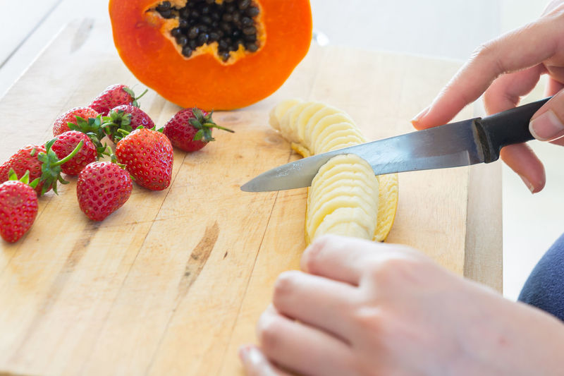 Close-up of hand holding fruits on cutting board