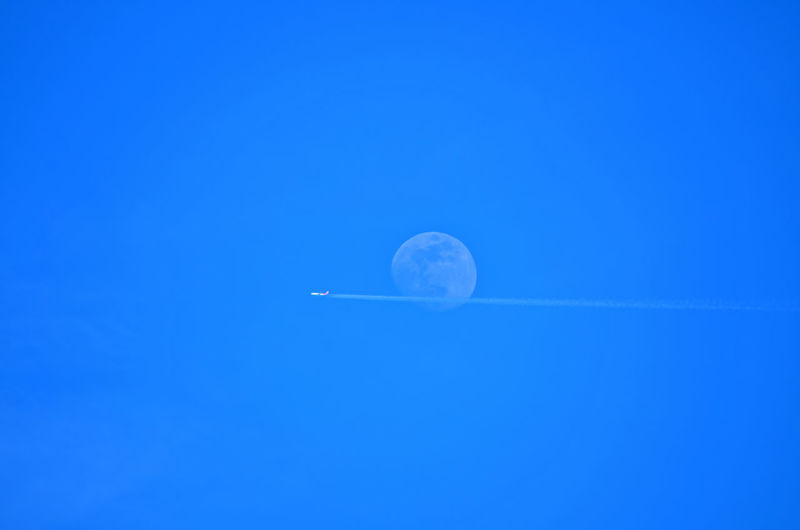 Low angle view of airplane flying in clear blue sky against moon
