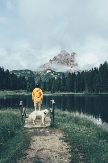 Rear view of man by dog standing against lake
