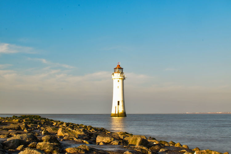 Lighthouse amidst sea and buildings against sky