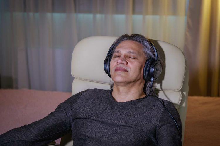 50-year-old man listens to music on headphones at home, sitting in a chair. relaxing delight.