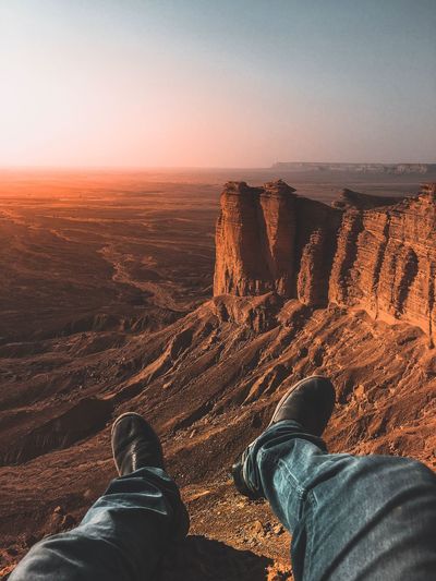 Low section of man sitting on landscape against sky during sunset