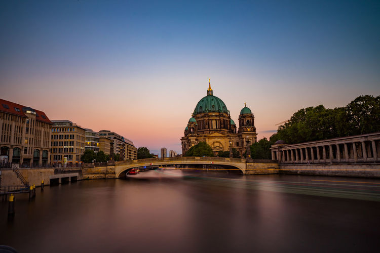 Light trail over river by berlin cathedral against clear sky during sunset