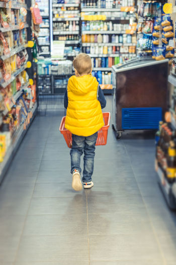Full length rear view of boy with bucket walking in supermarket