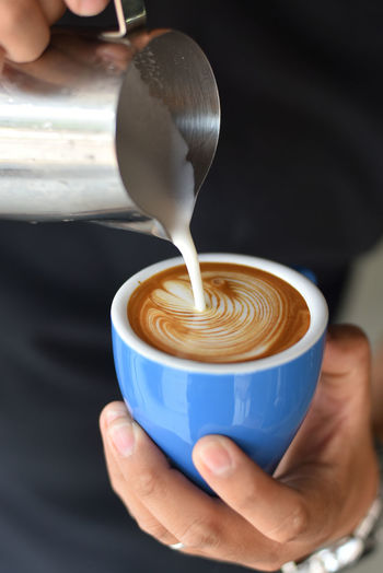 Close-up of hand pouring milk in coffee