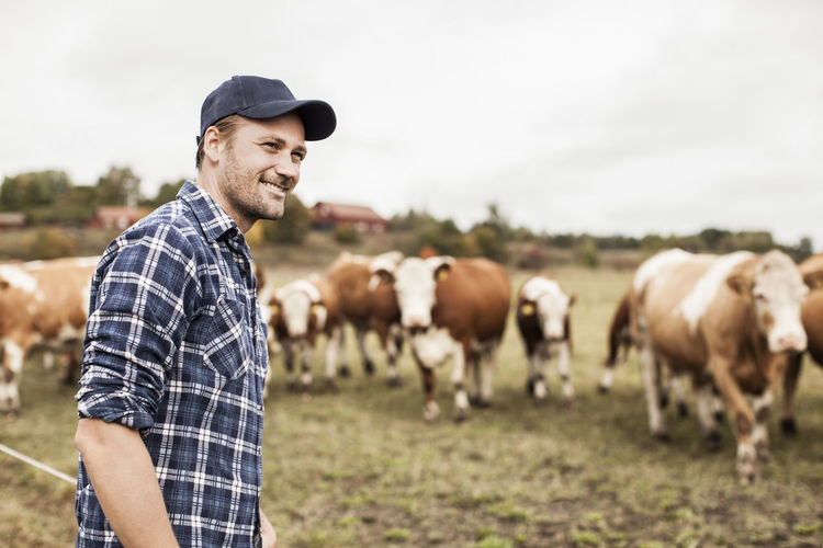 Smiling farmer looking away at field while animals grazing in background