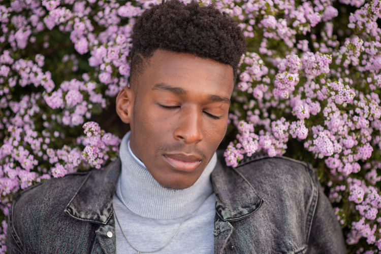 Young man with eyes closed against pink flowers