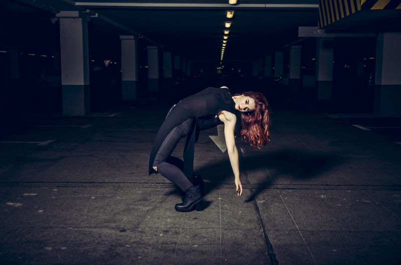 Redhead woman bending over backwards in parking lot at night