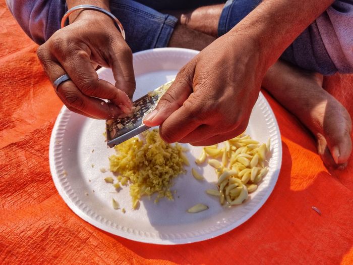 Midsection of person preparing garlic clove on a plate using hand.