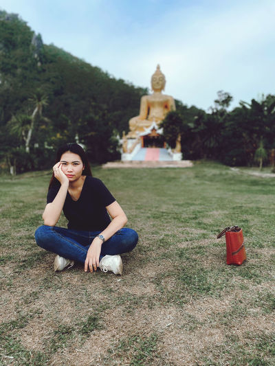 Portrait of young woman sitting on grass against sky