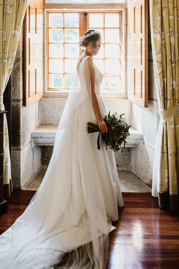 Full length of bride holding bouquet standing at home