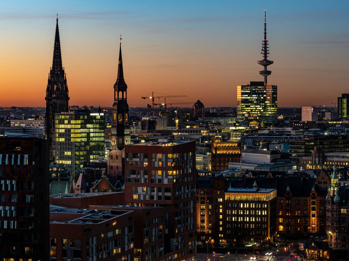 Illuminated buildings in city against sky during sunset