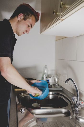 Side view of young man washing utensils in kitchen