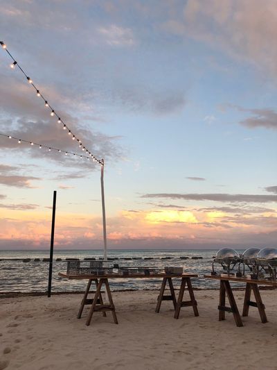 Tables on beach against sky during sunset