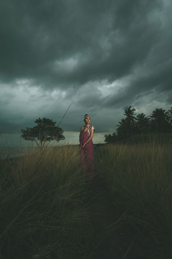 Full length of woman standing on field against storm clouds